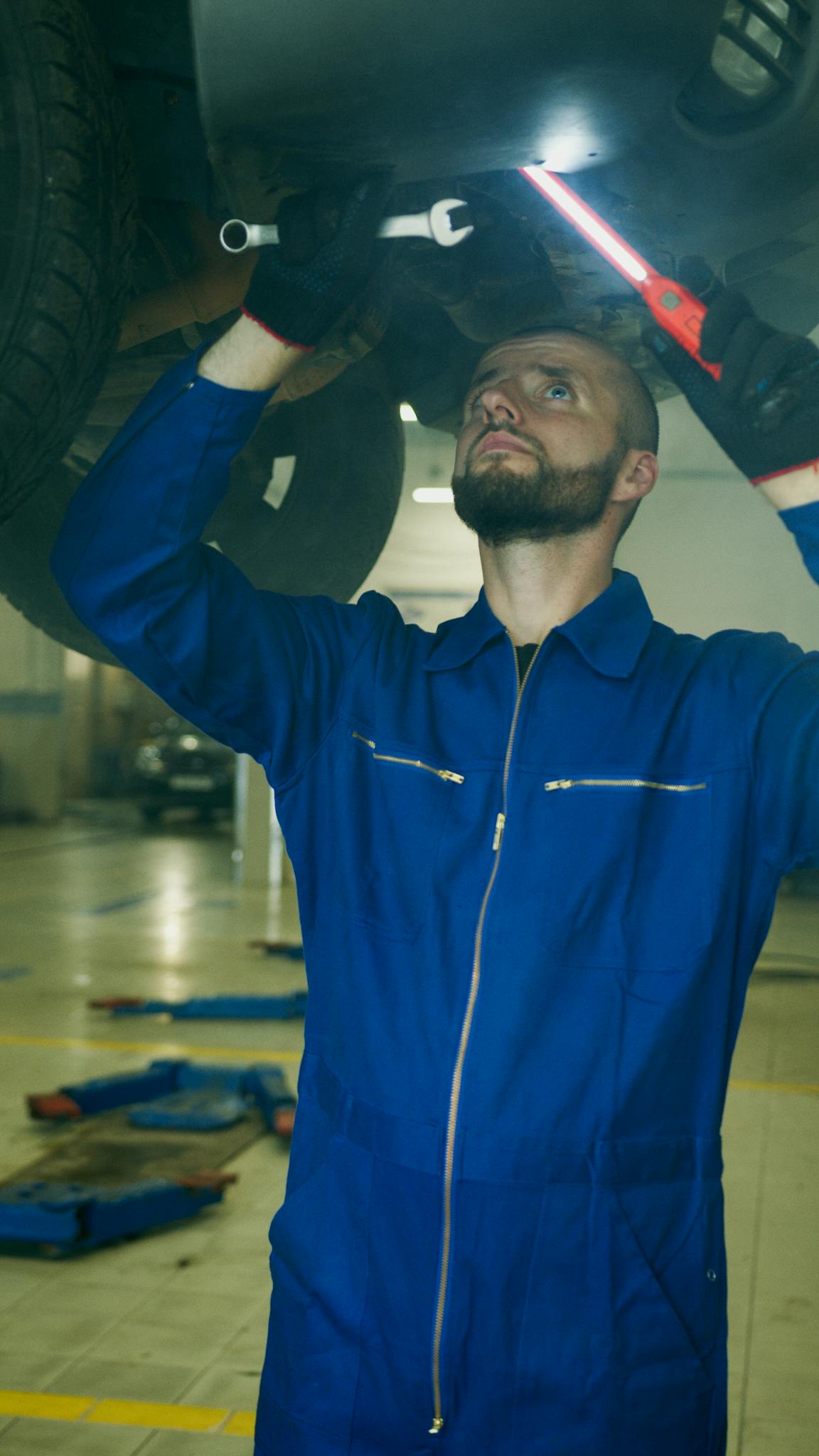 Mechanic in blue coveralls working under a car, providing maintenance and inspection services.